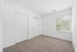 Bright, spacious empty bedroom with fresh carpet and a large window offering natural light and a serene view.