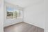 Bright room with large window offering garden views, featuring sleek hardwood flooring and fresh white walls.