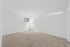 Bright, minimalist room with soft carpet flooring, natural light filtering through a window, and a sleek floor lamp.