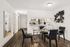 Modern dining area with sleek black chairs, glass table, and open kitchen view, enhanced by elegant wood flooring and contemporary artwork.