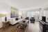 Modern living room with elegant wooden flooring, comfortable sofa, stylish decor, and floor-to-ceiling windows offering natural light.