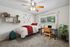 Cozy bedroom with plush carpeting, a comfy bed with red accents, modern desk setup, lush green plant, and ample natural light through a large window.