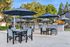 Charming outdoor patio area with chic dining tables, large umbrellas, and modern grills, surrounded by lush greenery and a playful children's area.