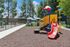 Vibrant playground featuring a colorful slide and climbing structure, surrounded by lush trees and picnic tables under umbrellas.