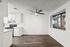 Chic apartment featuring a modern kitchen with white cabinetry, sleek appliances, and an open dining area with hardwood floors, enhanced by a ceiling fan and large window views.