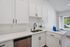 Modern kitchen with sleek white cabinets, elegant black fixtures, and abundant natural light from a large window.