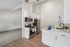 Modern kitchen with sleek stainless steel appliances, bright white cabinets, and elegant wood flooring, adjacent to a cozy, carpeted living area.