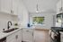 Bright, modern kitchen with sleek white cabinets, elegant countertops, and stainless steel appliances, featuring a large window with a beautiful view.