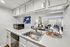 Bright kitchen with sleek white cabinetry, overlooking a stylish living room with modern decor and large glass doors leading to a scenic view.
