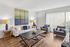 Sophisticated living room with elegant decor, featuring a modern beige sofa, chic armchairs, large abstract artwork, and floor-to-ceiling windows with natural light.