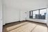 Bright apartment room with hardwood floors and large window offering stunning city and water views.