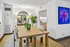 Elegant dining area featuring a wooden table with stylish green glassware, accented by a large mirror and vibrant artwork, adjacent to a modern kitchen.