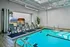 Luxurious indoor pool area with sleek lounge chairs, modern sauna, and vibrant potted plant, offering a serene retreat.