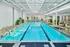 Bright indoor pool area with stylish skylights, elegant flooring, and cozy seating surrounded by lush greenery.