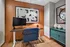 Chic home office space with modern artwork, ergonomic desk, and stylish blue chair, set against a warm orange accent wall.