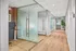 Modern office hallway with elegant glass walls, a stylish workspace, and warm wooden flooring.