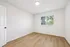 Bright and airy room with sleek wooden floors and a large window offering charming garden views, perfect for a cozy bedroom retreat.