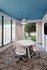 Modern meeting room with chic white furnishings, vibrant blue ceiling, and large windows offering lush garden views.