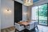 Elegant dining area with contemporary lighting, stylish wooden table, and large window offering scenic garden views.