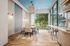 Contemporary communal dining space with stylish lighting, large windows showcasing scenic greenery, and elegant wooden flooring.