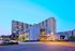 Elegant apartment complex at dusk with modern architecture, illuminated windows, lush landscaping, and ample parking.