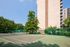 Modern apartment building with adjacent tennis courts surrounded by lush greenery under a clear blue sky.
