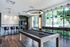 Elegant lounge area with a sleek pool table, contemporary bar seating, and panoramic windows offering lush garden views.
