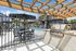Elegant outdoor patio with modern grilling area, stylish seating, and refreshing pool under a pergola with blue skies.