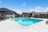 Inviting apartment outdoor area with a pristine swimming pool, chic sun loungers, and modern architecture under a bright blue sky.