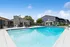 Inviting outdoor pool area with modern seating, surrounded by lush greenery and a clubhouse under a clear blue sky.