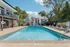 Inviting apartment complex featuring a sparkling outdoor pool with modern lounge chairs, surrounded by lush greenery and charming buildings.