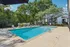 Inviting apartment community pool surrounded by lush green trees and modern lounge chairs under a clear blue sky.