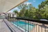 Charming apartment balcony view of a sparkling pool surrounded by lush greenery and modern buildings, offering a tranquil, scenic retreat.