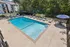 Inviting outdoor pool area with relaxing lounge chairs and umbrellas, surrounded by lush greenery and modern apartment buildings.