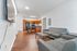 Modern apartment interior showcasing an open-concept living area with sleek gray sofas, wooden flooring, and a stylish kitchen with wooden cabinets.