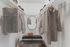 Spacious walk-in closet with neatly arranged clothes, a mirror, bench, and handbags.