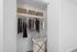 Chic white closet with wooden hangers, organized clothing, and woven baskets.