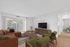 Bright living room with modern decor, featuring a large window, brown leather sofa, wood furniture, and green accent chairs.