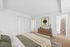 Inviting bedroom with a cozy bed, soft green bedding, wooden dresser, and abstract wall art, leading to a bathroom with a patterned shower curtain.
