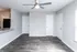 Modern living room with sleek wood flooring and a ceiling fan, adjacent to a kitchen area.