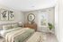 Inviting bedroom with modern decor featuring a king-sized bed, stylish green and beige bedding, natural wood furnishings, and a window with airy curtains.