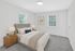 Bright and cozy bedroom with plush carpeting, featuring a stylish bed, modern nightstand with lighting, and large windows for natural light.