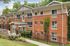 Charming red-brick apartment complex surrounded by lush greenery, featuring large windows and elegant entryway.