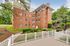 Charming brick apartment building with lush greenery and inviting white picket fencing, nestled in a serene and picturesque setting.