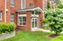 Elegant apartment entrance with modern brick design, lush landscaping, and a welcoming glass door.