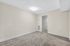 Bright, freshly painted room with cozy carpeting and modern recessed lighting, leading to a sleek hallway with a stylish white door.