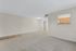 Inviting living space with plush carpet, modern lighting, and a glimpse into a cozy kitchen area with warm wooden cabinetry.