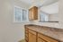 Bright kitchen nook with natural light and sleek countertops, featuring warm wood cabinetry and a charming passthrough window.