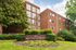 Charming exterior of Manchester Manor, a red-brick apartment building surrounded by lush greenery and vibrant flower beds.