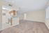Bright and airy open-concept living space with plush carpeting, featuring a modern kitchen with wooden cabinetry and sleek appliances.